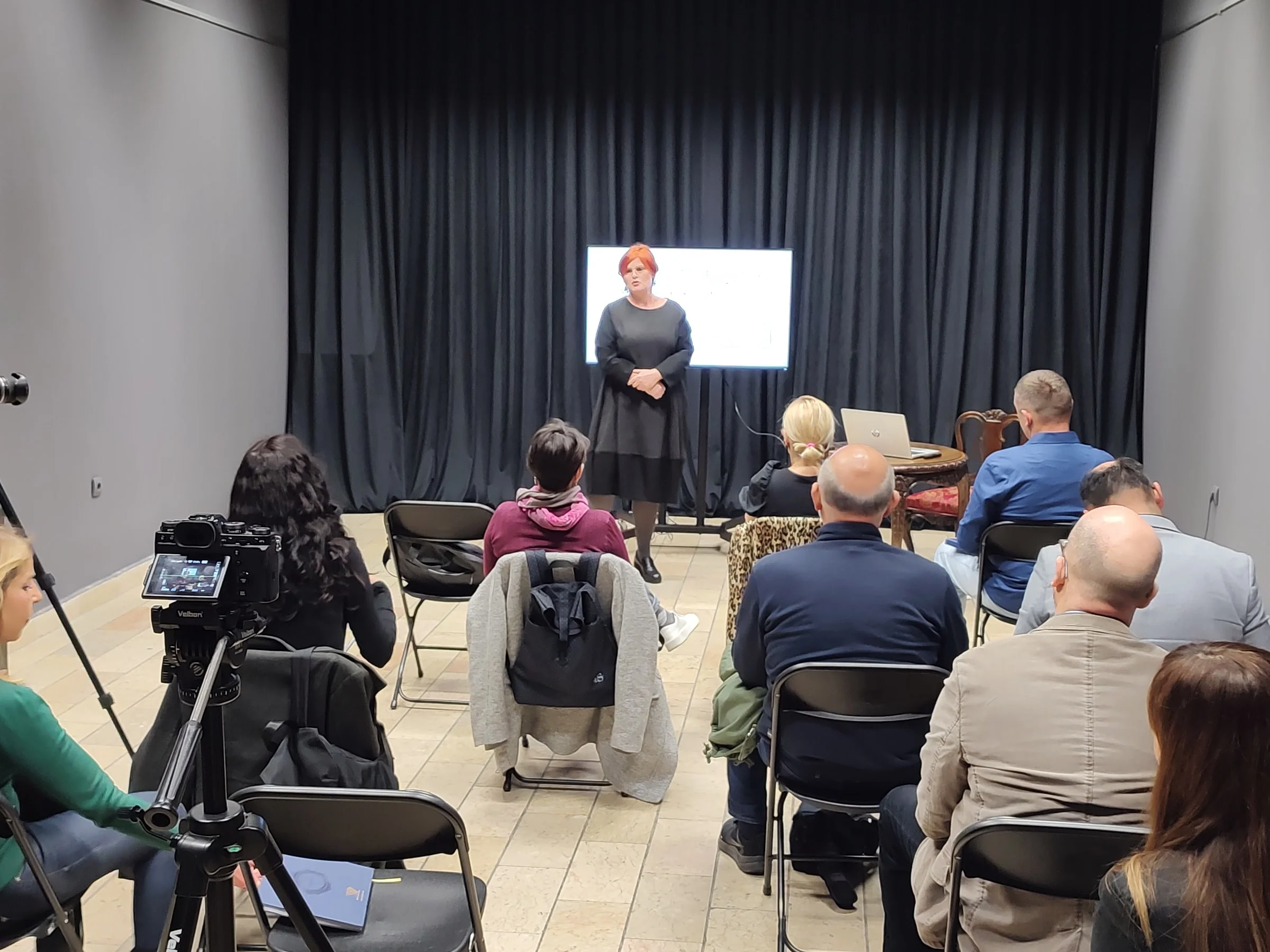 A speaker addresses participants of a workshop on accessible media programmes, with a camera recording in the foreground.